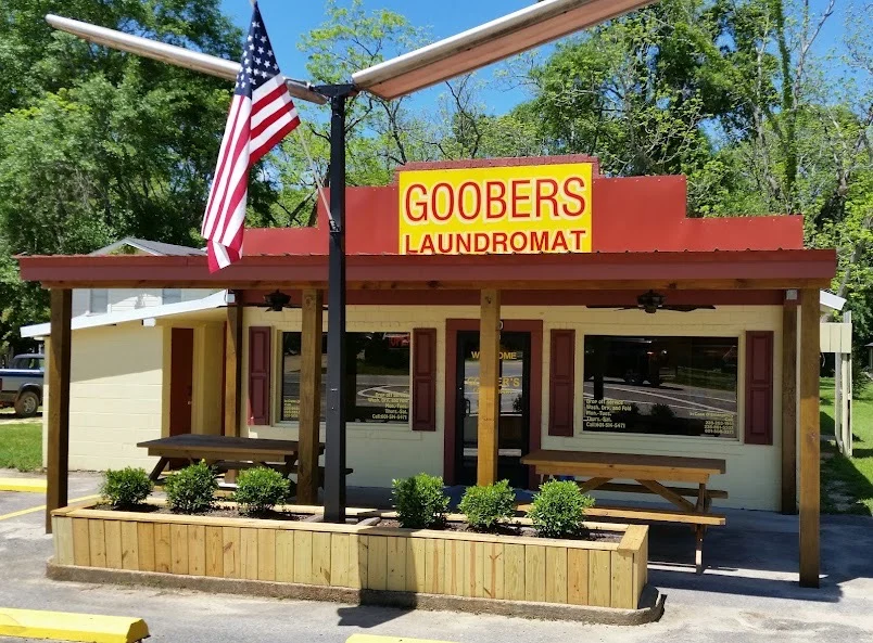 Goobers Laundromat's yellow sign, American flag, and covered front porch with picnic tables
